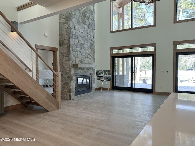 unfurnished living room featuring a high ceiling, a fireplace, wood finished floors, and baseboards