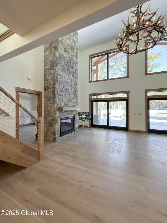 unfurnished living room with an inviting chandelier, a high ceiling, wood finished floors, and a stone fireplace