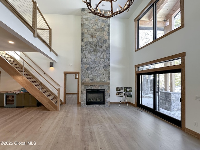 unfurnished living room with baseboards, stairway, an inviting chandelier, a stone fireplace, and light wood-style floors