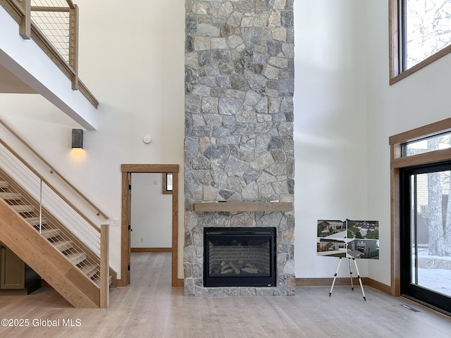 unfurnished living room featuring light wood-style flooring, a fireplace, a high ceiling, and visible vents