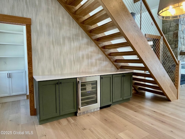 bar featuring light wood-style flooring, beverage cooler, and stairway