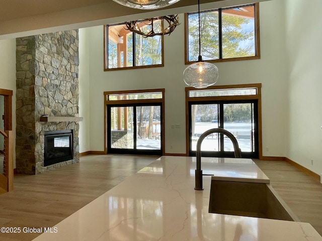 interior space with a stone fireplace, wood finished floors, a towering ceiling, and baseboards