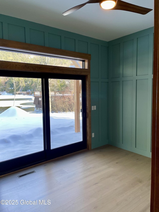 unfurnished room with light wood finished floors, visible vents, a decorative wall, and a ceiling fan