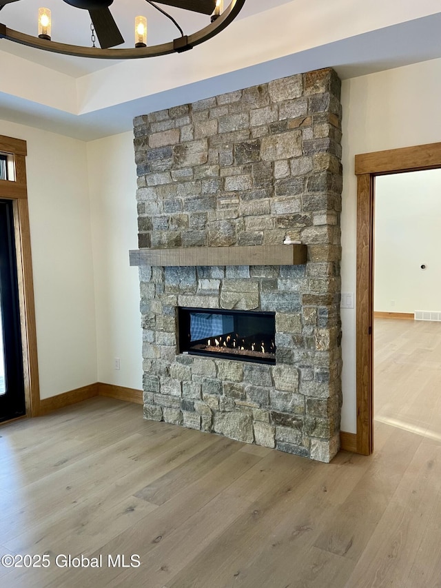 unfurnished living room with a stone fireplace, wood finished floors, visible vents, baseboards, and a tray ceiling