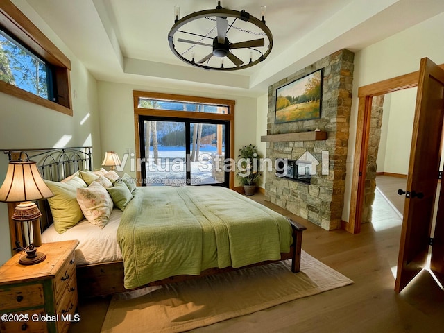 bedroom with french doors, a tray ceiling, light wood-style flooring, and access to exterior