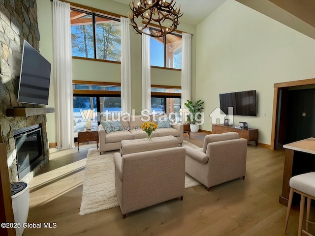 living room featuring a towering ceiling, light wood-style flooring, a wealth of natural light, and a stone fireplace