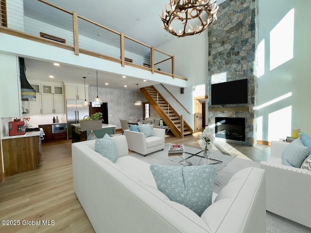 living area featuring a fireplace, light wood finished floors, a towering ceiling, an inviting chandelier, and stairs