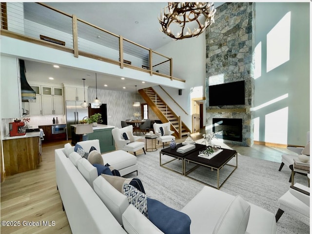 living room featuring a notable chandelier, a fireplace, light wood finished floors, a high ceiling, and stairs