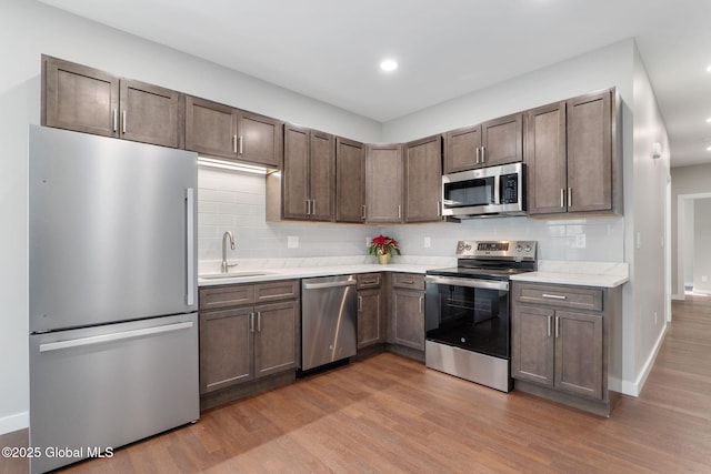 kitchen with backsplash, sink, light wood-type flooring, appliances with stainless steel finishes, and dark brown cabinets