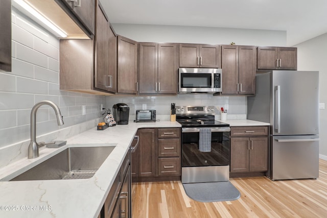 kitchen with light stone countertops, stainless steel appliances, decorative backsplash, sink, and light hardwood / wood-style floors