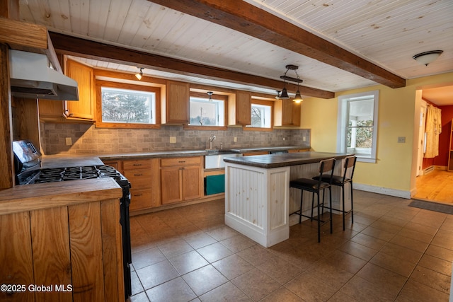 kitchen with decorative light fixtures, backsplash, gas stove, a center island, and wall chimney exhaust hood