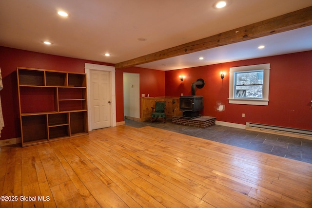 unfurnished living room featuring a baseboard heating unit, beam ceiling, a wood stove, and hardwood / wood-style flooring