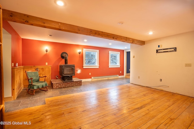 unfurnished room with light hardwood / wood-style floors, a wood stove, and a baseboard heating unit