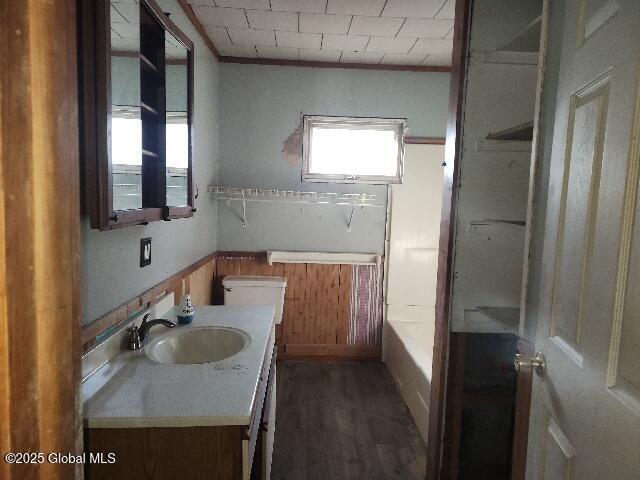 bathroom with vanity, a tub, ornamental molding, a wainscoted wall, and toilet