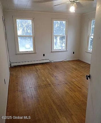empty room with baseboard heating, ornamental molding, dark hardwood / wood-style floors, and ceiling fan