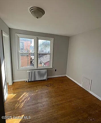 unfurnished room featuring dark wood-type flooring and radiator heating unit