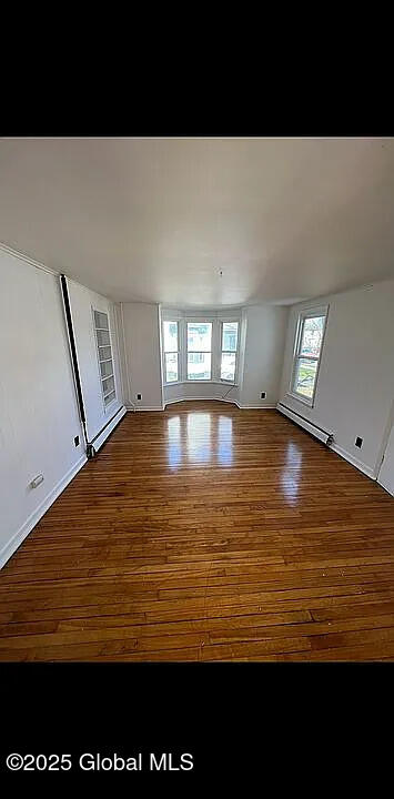 unfurnished room featuring plenty of natural light, wood-type flooring, and a baseboard radiator