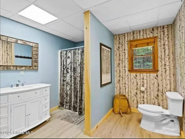 bathroom with a paneled ceiling, wood-type flooring, vanity, toilet, and walk in shower