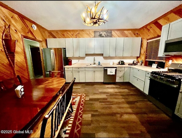 kitchen with appliances with stainless steel finishes, pendant lighting, wooden walls, sink, and a chandelier