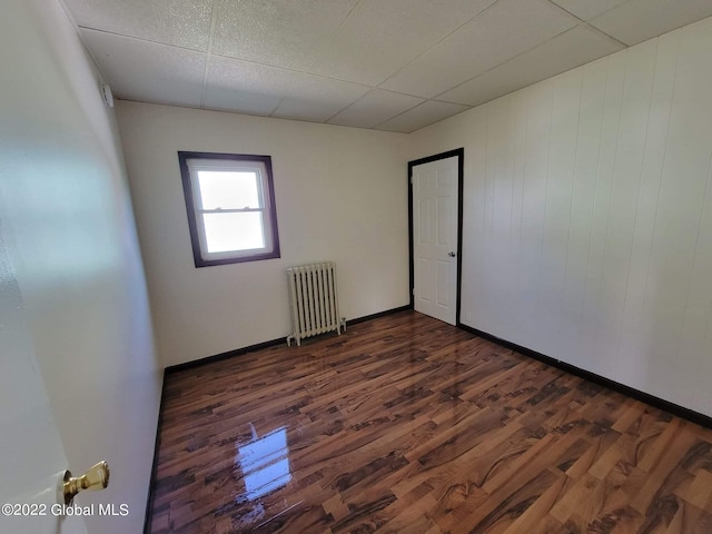 empty room featuring radiator heating unit, dark hardwood / wood-style flooring, and a drop ceiling