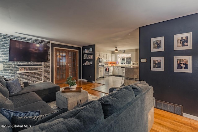 living room with ceiling fan, brick wall, sink, and light wood-type flooring