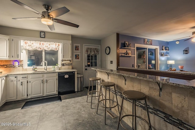 kitchen featuring a breakfast bar, white cabinetry, dishwasher, sink, and light stone counters