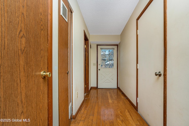 corridor with visible vents, baseboards, a textured ceiling, and hardwood / wood-style floors