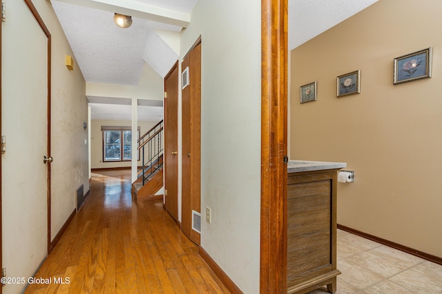 hall with stairway, baseboards, a textured ceiling, and visible vents