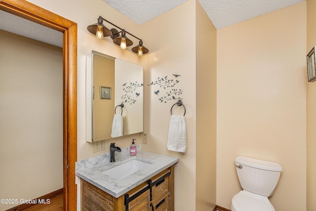 half bathroom with vanity, toilet, baseboards, and a textured ceiling