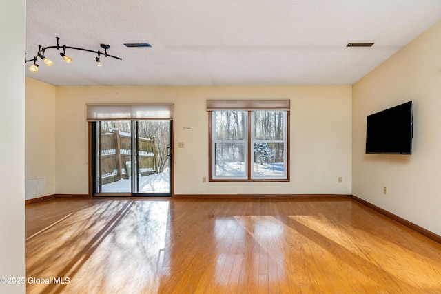 unfurnished living room featuring hardwood / wood-style floors, rail lighting, baseboards, and a textured ceiling