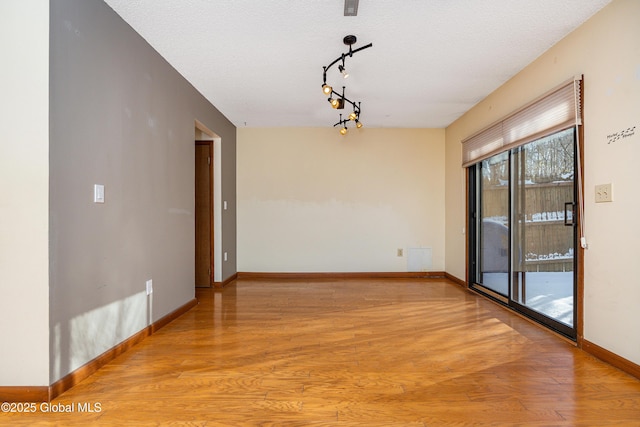 spare room featuring light wood finished floors, rail lighting, a textured ceiling, and baseboards