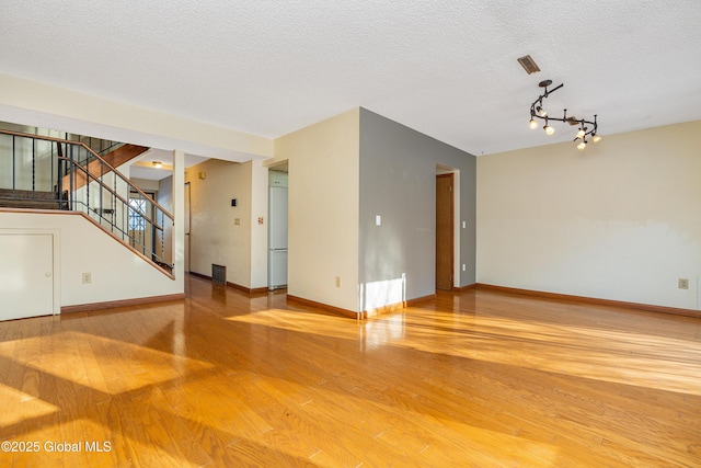 unfurnished room with stairway, wood finished floors, baseboards, and a textured ceiling