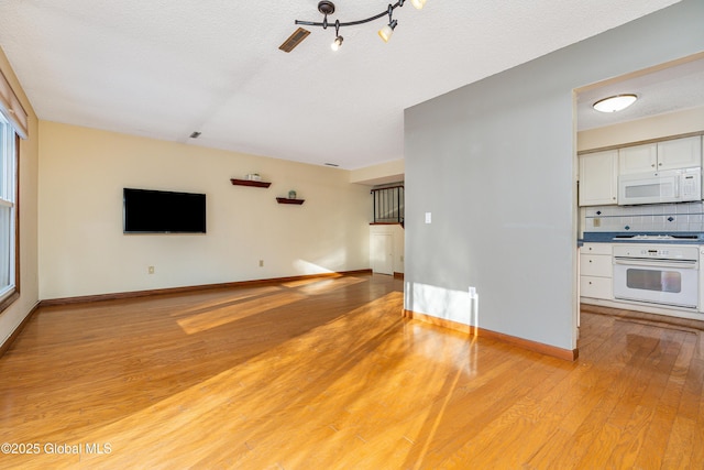 unfurnished living room with light wood-style flooring, baseboards, and a textured ceiling