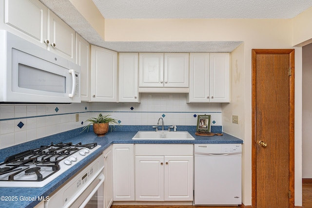 kitchen with a sink, backsplash, dark countertops, white cabinetry, and white appliances