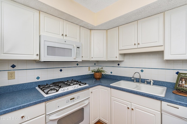 kitchen with dark countertops, backsplash, white cabinets, white appliances, and a sink