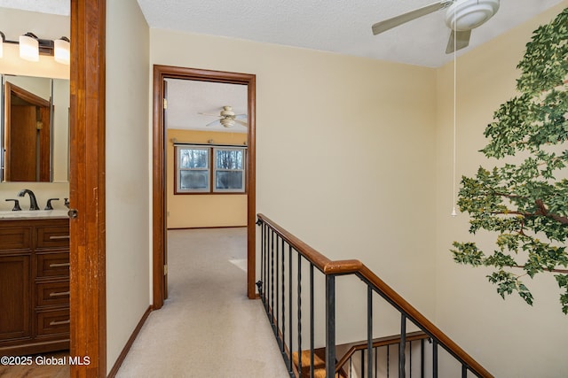 corridor with light colored carpet, a textured ceiling, baseboards, and a sink