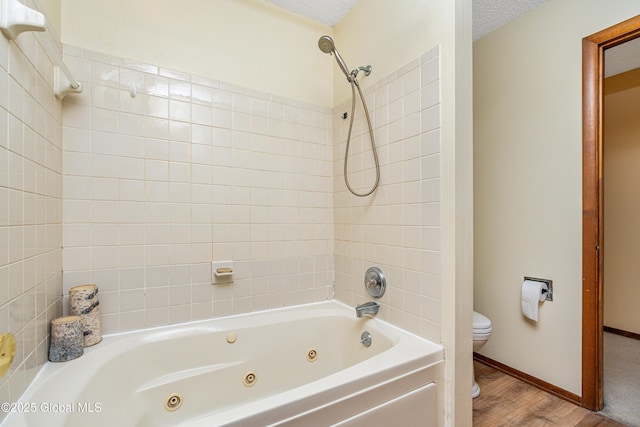 bathroom with toilet, a combined bath / shower with jetted tub, a textured ceiling, wood finished floors, and baseboards