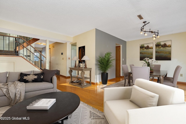 living room with stairs, baseboards, light wood finished floors, and a textured ceiling