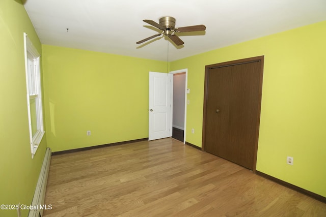 unfurnished bedroom with a baseboard radiator, ceiling fan, light wood-type flooring, and a closet