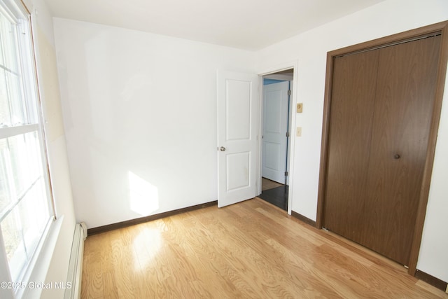 unfurnished bedroom with a baseboard radiator, light hardwood / wood-style floors, and a closet