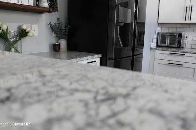 kitchen featuring light stone counters, backsplash, refrigerator with ice dispenser, and white cabinets