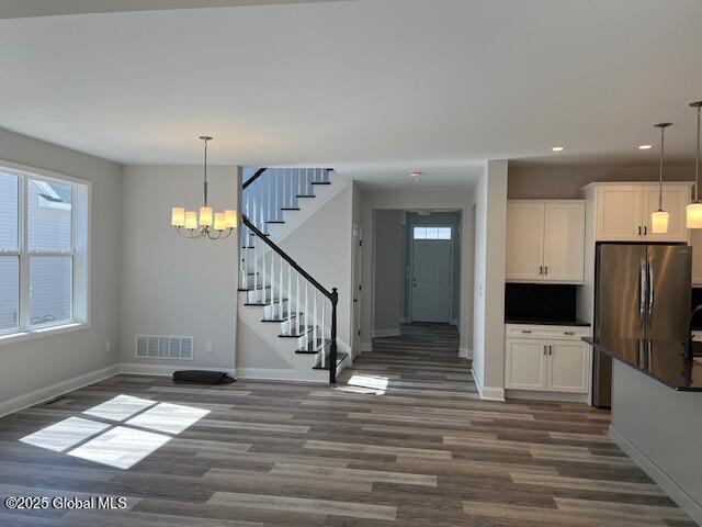 interior space with stainless steel fridge, decorative light fixtures, dark wood-type flooring, a chandelier, and white cabinets