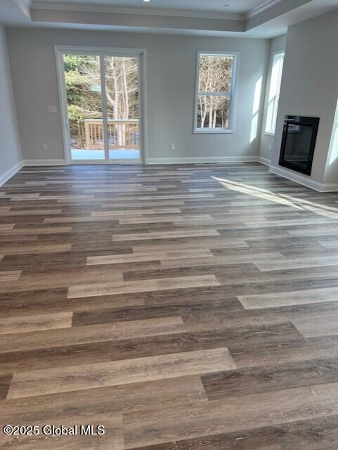 unfurnished living room featuring plenty of natural light, a tray ceiling, ornamental molding, and hardwood / wood-style flooring