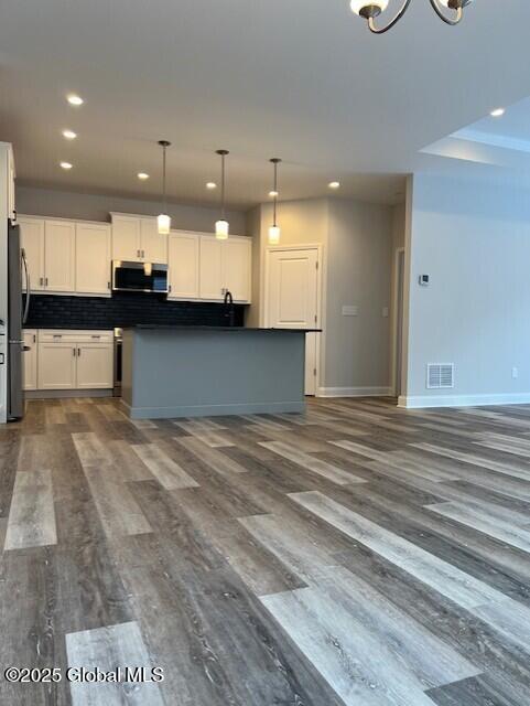 kitchen featuring decorative light fixtures, white cabinetry, dark hardwood / wood-style flooring, stainless steel appliances, and backsplash