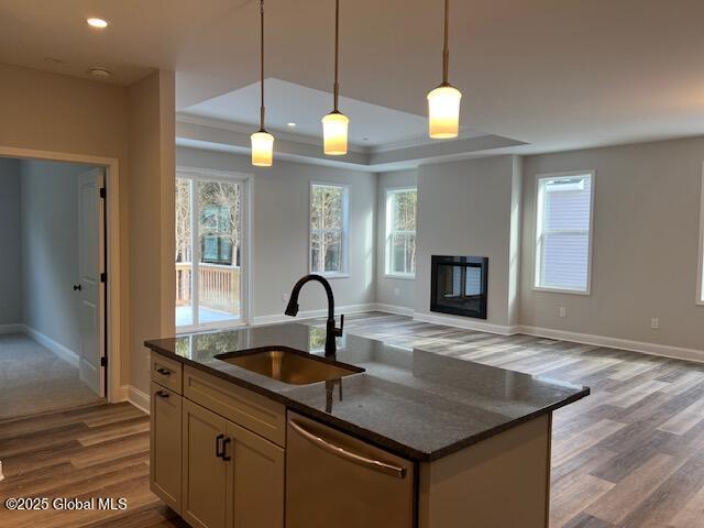 kitchen with decorative light fixtures, stainless steel dishwasher, dark stone counters, sink, and a tray ceiling