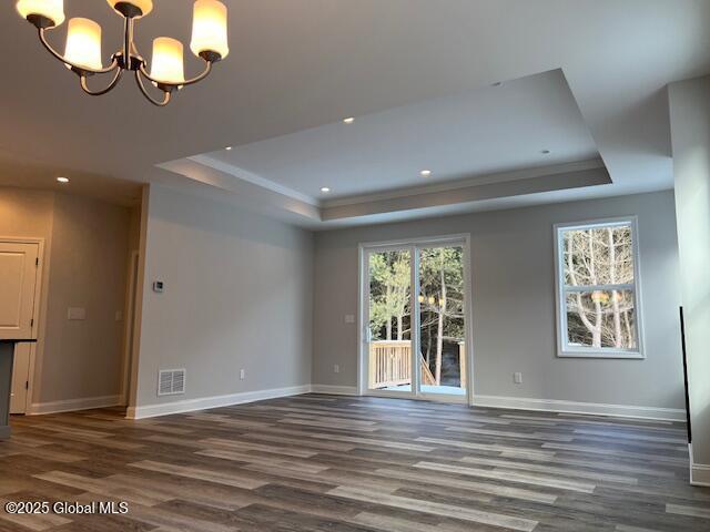 unfurnished room with dark wood-type flooring, an inviting chandelier, and a tray ceiling