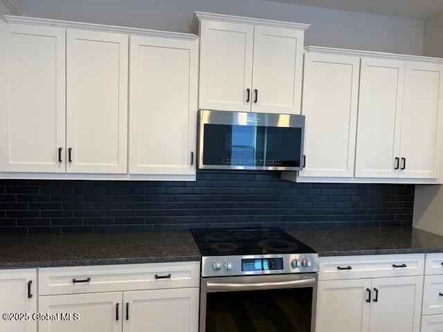 kitchen with appliances with stainless steel finishes, backsplash, white cabinets, and dark stone counters