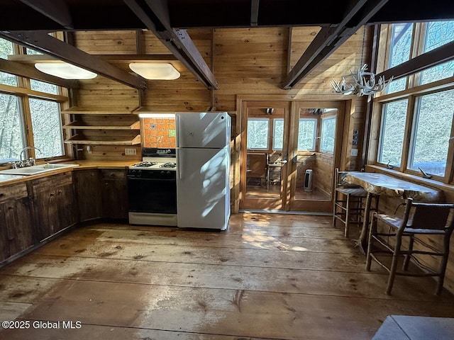 kitchen with white appliances, wood walls, a sink, open shelves, and light wood finished floors