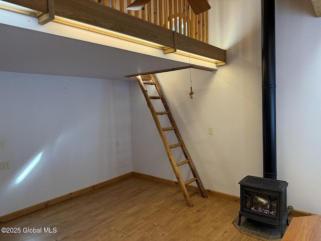 basement with stairs, a wood stove, baseboards, and wood finished floors