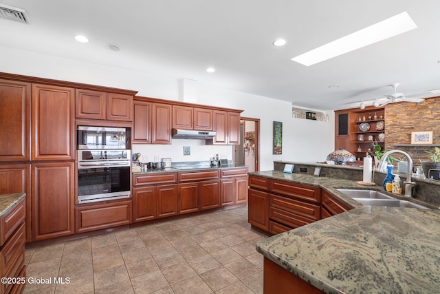 kitchen with sink, ceiling fan, a skylight, stainless steel appliances, and stone countertops